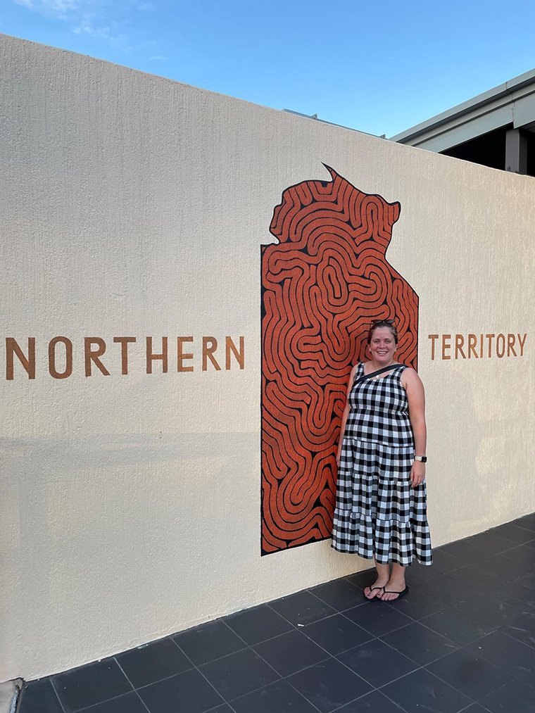Woman Rachael Vincennt against a small wall with a sign saying Northern Territory
