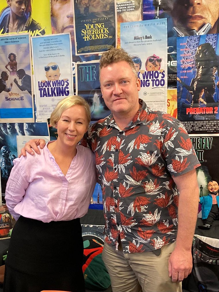 Woman Jasmine Stanton and man Dr Bernie Westley standing in front of wall with posters