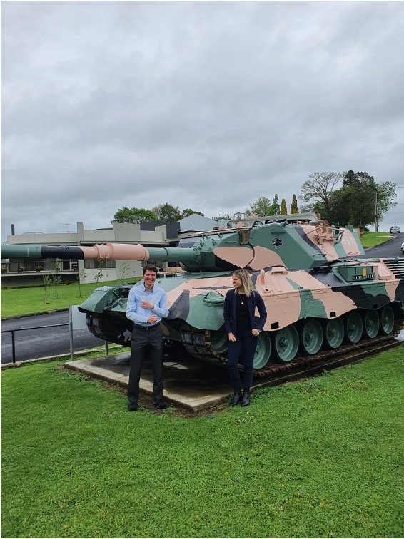 Smiling woman and smiling man in front of a tank