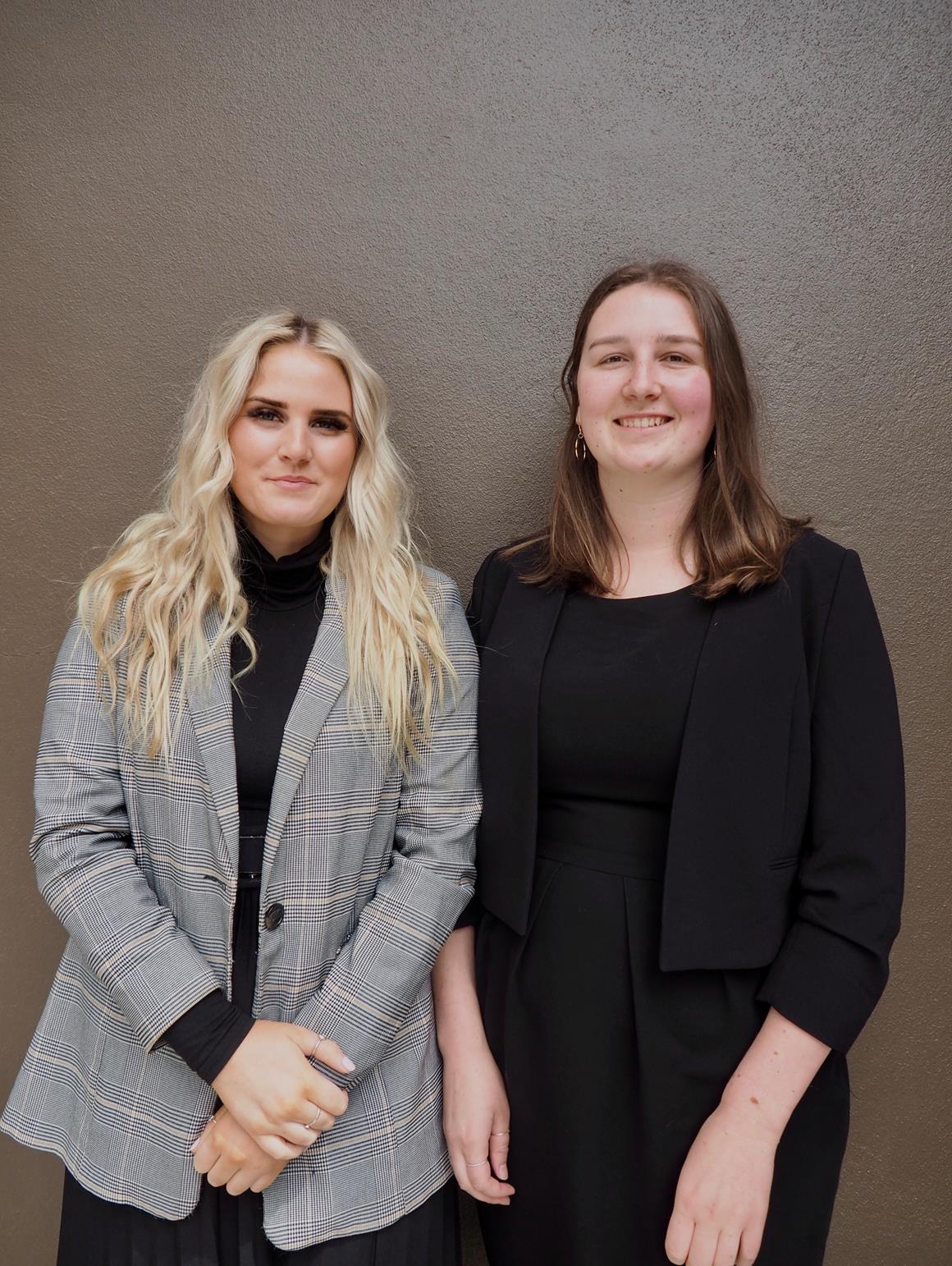 Two women standing against a plain wall